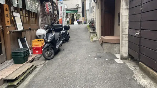 A narrow street in Shinjuku with wooden shops and parked motorbikes